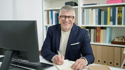 Poster - Middle age grey-haired man teacher using computer writing on notebook at university classroom