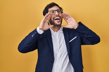 Poster - Handsome latin man standing over yellow background smiling cheerful playing peek a boo with hands showing face. surprised and exited