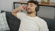 © Krakenimages.com - Young arab man listening to music sitting on sofa at home
