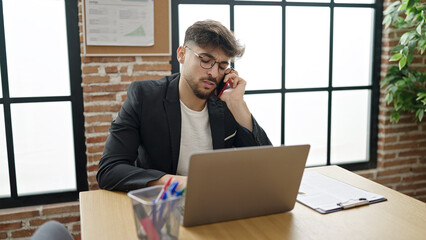 Wall Mural - Young arab man business worker using laptop talking on smartphone at office