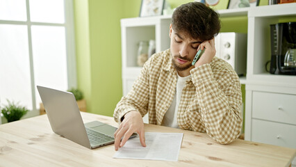 Canvas Print - Young arab man talking on smartphone reading document at home