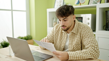 Wall Mural - Young arab man using laptop reading document at home