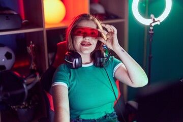 Poster - Young redhead woman streamer playing video game using virtual reality glasses at gaming room