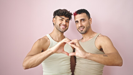 Wall Mural - Two men couple hugging each other doing heart gesture over isolated pink background