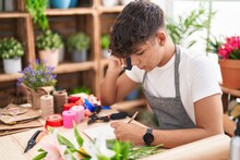 Young Hispanic Teenager Florist Talking On Smartphone Writing On Notebook At Flower Shop