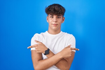 Hispanic teenager standing over blue background pointing to both sides with fingers, different direction disagree