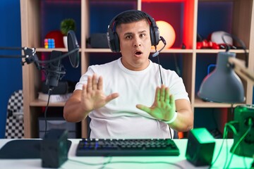 Poster - Young hispanic man playing video games moving away hands palms showing refusal and denial with afraid and disgusting expression. stop and forbidden.