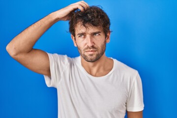 Sticker - Hispanic young man standing over blue background confuse and wondering about question. uncertain with doubt, thinking with hand on head. pensive concept.