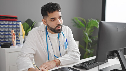 Poster - Young hispanic man doctor using computer writing notes at clinic