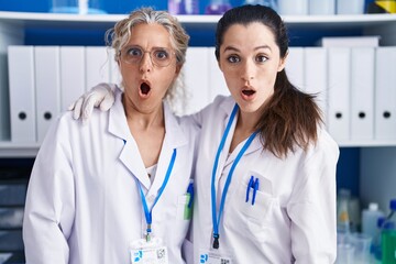 Poster - Mother and daughter working at scientist laboratory scared and amazed with open mouth for surprise, disbelief face