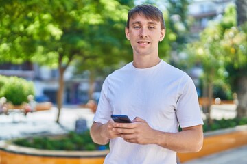 Wall Mural - Young caucasian man smiling confident using smartphone at park