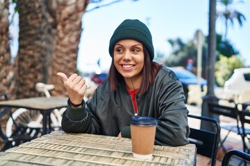 Sticker - Young hispanic woman drinking a cup of coffee outdoors pointing thumb up to the side smiling happy with open mouth