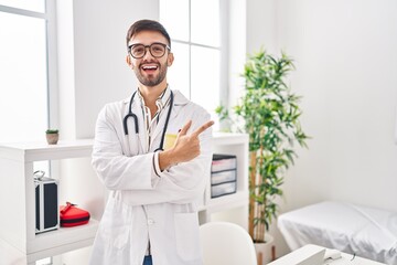 Poster - Hispanic man wearing doctor uniform and stethoscope smiling cheerful pointing with hand and finger up to the side