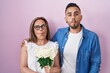 Hispanic mother and son together holding bouquet of white flowers making fish face with mouth and squinting eyes, crazy and comical.