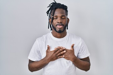 Wall Mural - African man with dreadlocks wearing casual t shirt over white background smiling with hands on chest with closed eyes and grateful gesture on face. health concept.