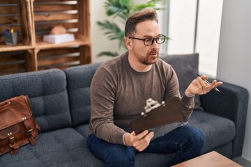 Poster - Young caucasian man psychologist sitting on sofa speaking at psychology clinic