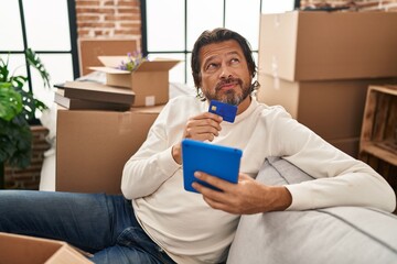 Sticker - Middle age man using touchpad and credit card sitting on sofa at new home