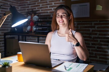 Wall Mural - Brunette woman working at the office at night doing happy thumbs up gesture with hand. approving expression looking at the camera showing success.