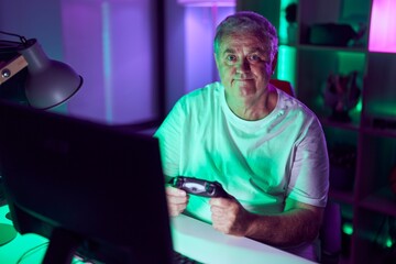 Poster - Middle age grey-haired man streamer playing video game using joystick at gaming room