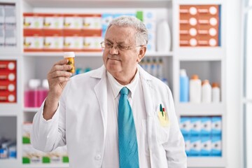 Poster - Middle age grey-haired man pharmacist smiling confident holding pills bottle at pharmacy