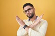 Hispanic young man wearing business clothes and glasses rejection expression crossing arms doing negative sign, angry face