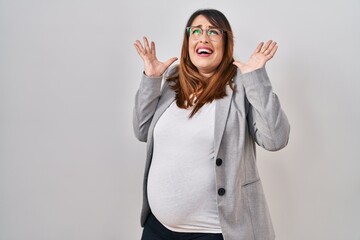 Canvas Print - Pregnant business woman standing over white background crazy and mad shouting and yelling with aggressive expression and arms raised. frustration concept.