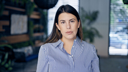 Wall Mural - Young beautiful hispanic woman standing with serious face at the office