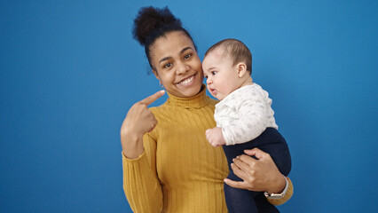 Wall Mural - Mother and son smiling confident pointing to baby over isolated blue background
