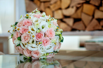 Gentle stylish wedding bouquet of roses and daisies on glass reflective surface in front of wooden logs, with copyspace