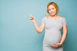 © AntonioDiaz - Studio shot of a pregnant woman pointing at copy space in a studio and looking happy