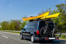 Back View Modern Black Family Wagon Van Car With Mounted Roof Kayak And Bike Tail Carrier Driving European Highway Road Against Blue Sky Summer Day. Lifestyle Travel Adventure Trip Journey Concept
