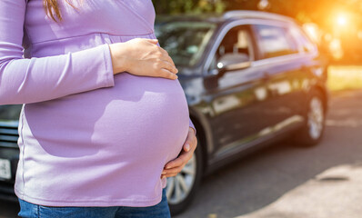 A pregnant girl with a big belly in a purple sweater on the background of a car. The concept of travel and a long trip in a car during pregnancy. Copy space for text