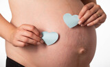 Fototapeta Na sufit - Two blue hearts on the background of the girl's pregnant belly. The concept of love for children and the birth of twin boys. Preparation for childbirth