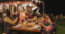 Big Family Celebrating Diwali: Indian Family In Traditional Clothes Gathered Together On A Dinner Table In A Backyard Garden Full Of Lights. Moment Of Happiness On A Hindu Holiday