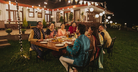 Big Indian Family Celebrating Diwali: Family Gathered Together on a Dinner Table in a Backyard Garden Full of Lights. Group of Adults Sharing Food, Laughs and Stories on a Hindu Holiday