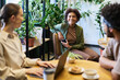 © pressmaster - Focus on young smiling African American businesswoman with smartphone looking at female colleague during discussion in cafe