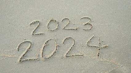 Wall Mural - message year 2023 replaced by 2024 written on beach sand background. goodbye 2023 hello to 2024 lapp