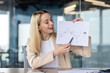 © Tetiana - A smiling young business woman holds in her hands and shows to the camera documents with work results, graphs, a project. Satisfied with the company's financial success