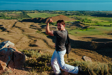 Canvas Print - Happy young man traveler showing his strength on top of the mountain