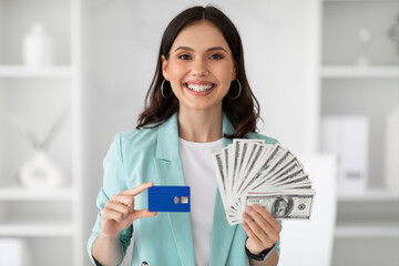 Wall Mural - Glad young european woman in suit shows credit card and lot of money, enjoy victory