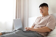 © Prostock-studio - Happy mature asian man using laptop in bed, copy space