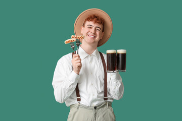 Young man in traditional German clothes with beer and sausages on green background