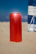 Czerwona puszka stojąca w piasku na plaży. W tle niebieskie niebo i parawan plażowy. 