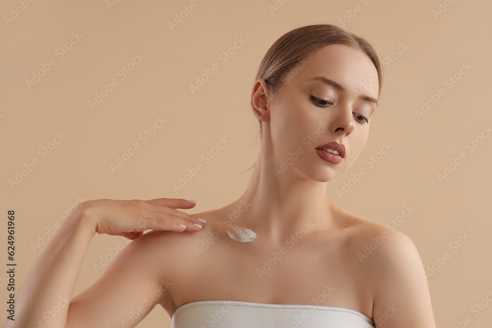 Pretty young woman with body cream on beige background