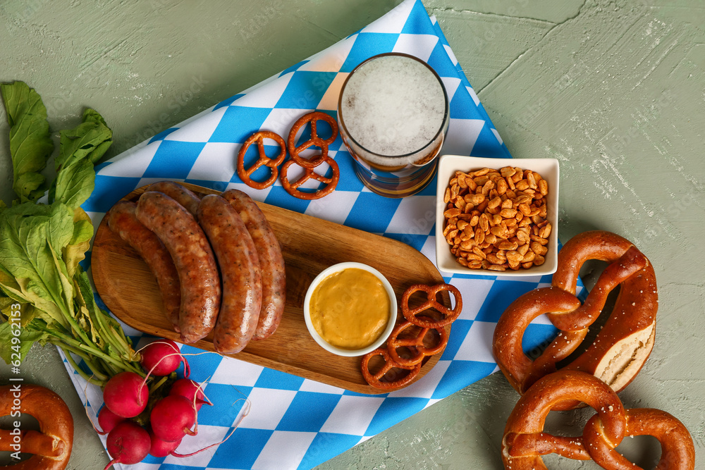 Glass of cold beer and board with different snacks on green background. Oktoberfest celebration