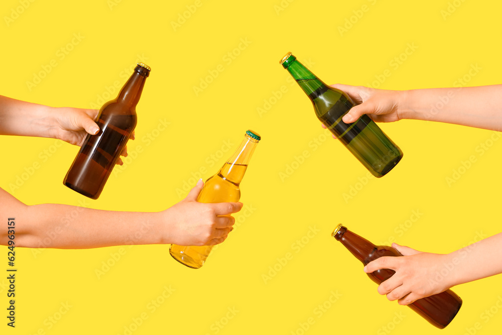 Female hands with bottles of cold beer on yellow background