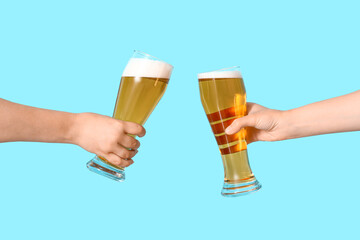 Female hands with glasses of cold beer clinking on blue background