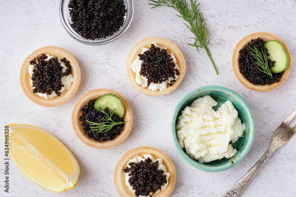Tasty tartlets with black caviar on light background