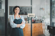© Satori Studio - Portrait of happy waitress standing at restaurant entrance with open sign, Portrait of young business woman attend new customers in her coffee shop.