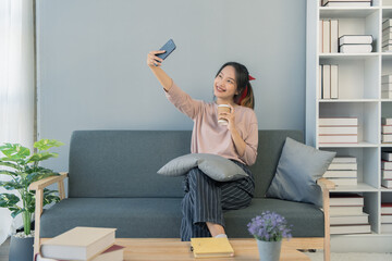 young woman sitting on a sofa with coffee cup and selfie in living room